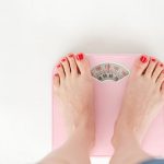Top view of crop anonymous barefoot female measuring weight on scales on white background